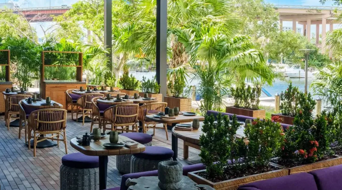 Terraza exterior de Tanuki River Landing con vista al río Miami entre vegetación.